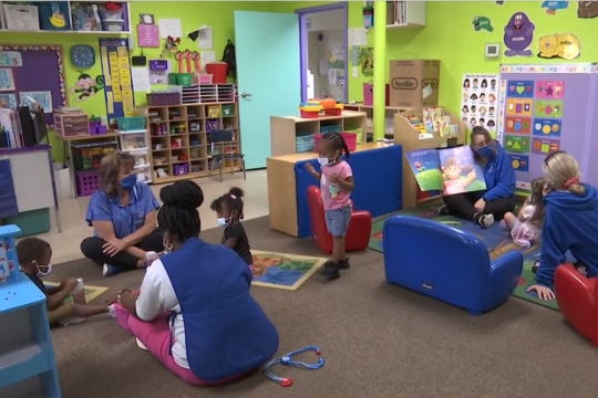 children and workers at a day care facilities sitting on the floor and playing.