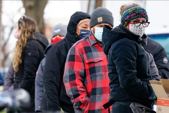 people wearing face masks waiting in a line outside.