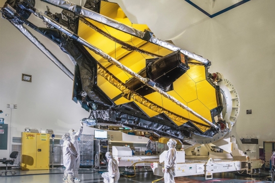 Four scientists in clean suits examine the folded James Webb Space Telescope