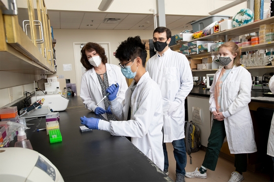 professor and students watching another student use a pipette.