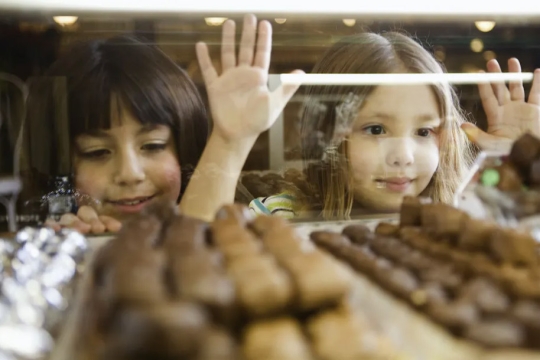 two children looking at a display case of chocolates.