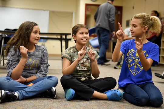 three children sitting on the floor using sign language.
