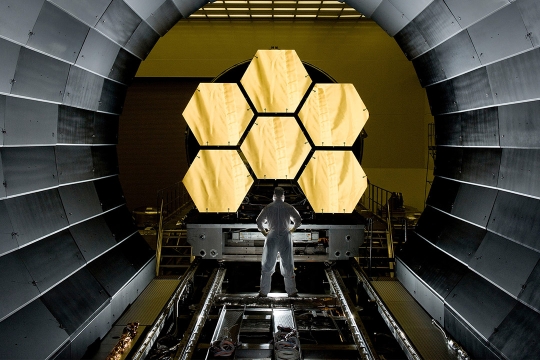 person standing in front of six hexagonal mirrors of the James Webb Space Telescope.