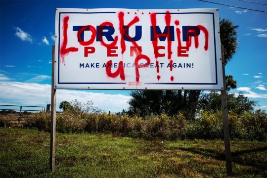 a Trump-Pence political billboard spray painted with Lock Him Up.