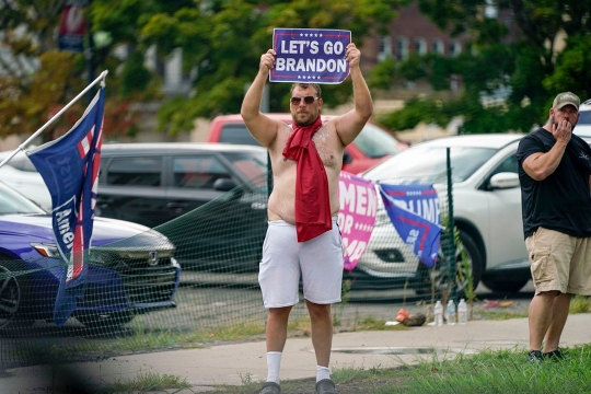 man standing near a sidewalk holding a sign that reads, Let's Go Brandon.