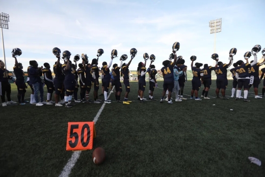 High school football players in a line with helmets raised.