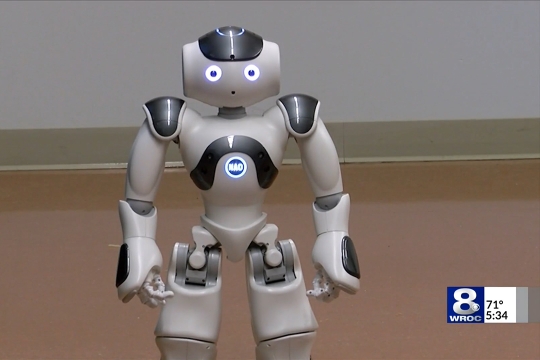 A picture of a small robot with glowing eyes and a logo on the chest that says, "NAO"