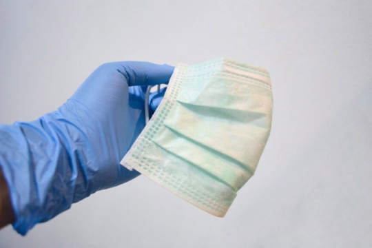 a gloved hand holding a disposable medical mask.