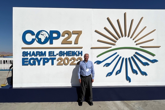 man standing outside in front of a sign that reads, COP27, Sharm El-Sheikh, Egypt, 2022.