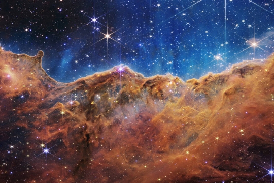 stars and a burnt orange gassy ridge in deep space.
