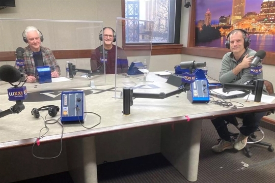 Three people with headphones on in front of microphones at the WXXI radio station.
