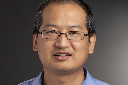 RIT professor, Yunbo Zhang wearing a light blue collared shirt and glasses.