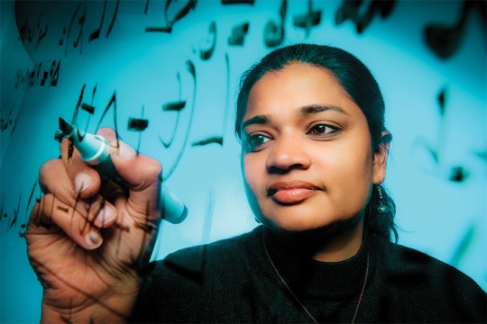 researcher writing with a marker on a clear surface toward the camera.