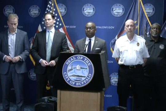 mayor of Buffalo standing behind a podium with four people standing on either side of him.