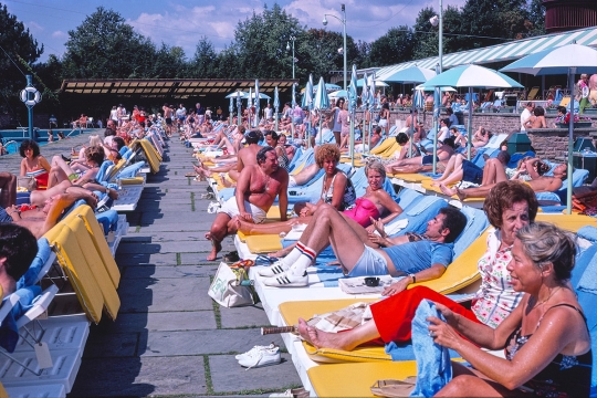 rows of people sunbathing in lounge chairs near a pool in the 1970s.