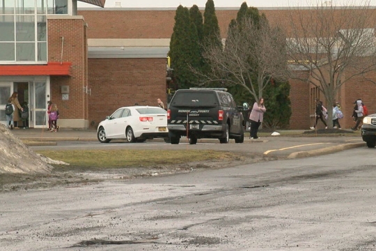 people, cars, and police car outside of a brick building.