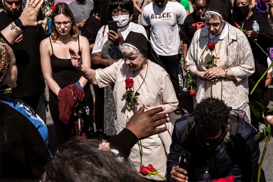 two nuns holding red roses with their hands extended as if blessing a crowd of people.