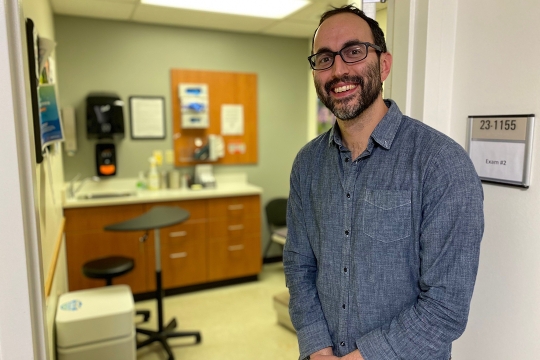 Man smiling, stands in front of a healthcare exam room.