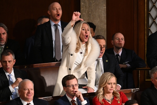 Person in a white jacket in congress showing a thumbs down with a disapproving expression.