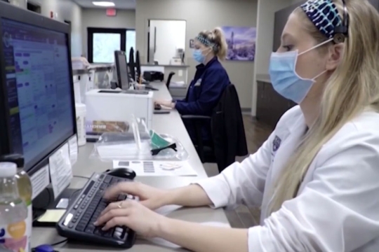 two nurses wearing masks working on computers.