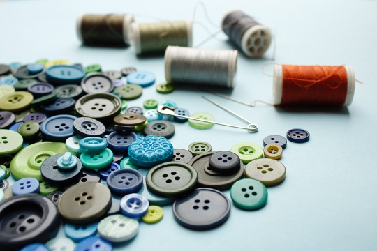 a pile of brown, green, and blue buttons next to a safety pin and five spools of thread.