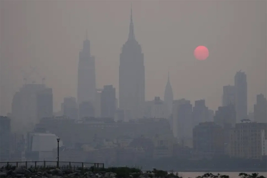 New York City skyline with the sun in the distance obscured by smog.