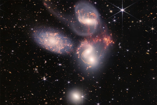 five galaxies surrounded by stars in space.