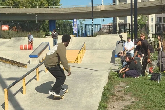 person skate boarding in a skate park while college students take photos off to the side.