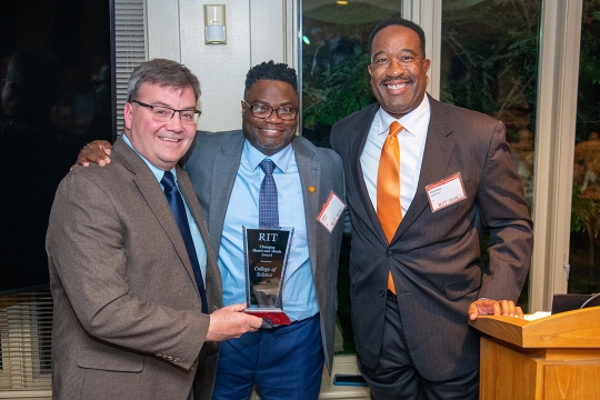 three college staff members posing with a glass award.