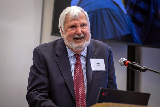man standing at a podium wearing a suit and smiling.