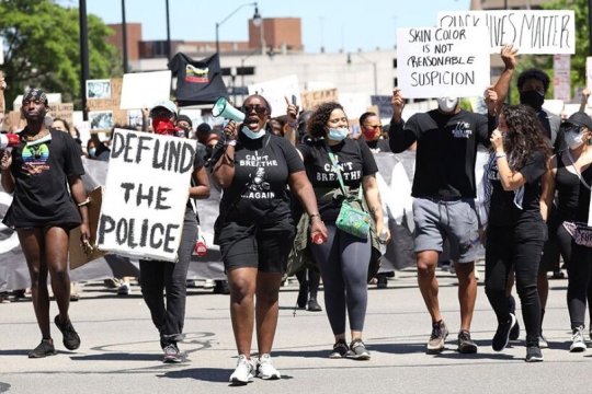 crowd of protestors walking down a street with signs that read, defund the police, and skin color is not reasonable suspicion.