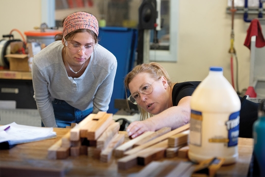 college student watching professor looking at a stack of wood lengthwise.