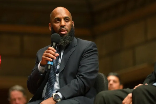 Irshad Altheimer is seated on a panel in a public forum.