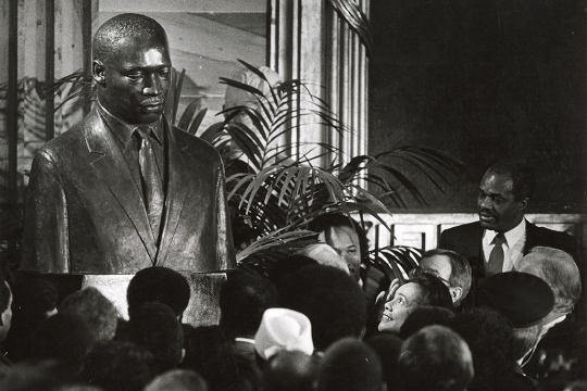 a black and white image of a group of people facing Coretta Scott King as she reacts to an MLK portrait being unveiled