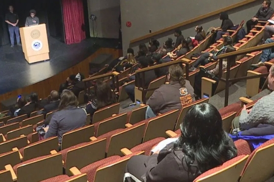 a student from Rochester Prep Charter School stands behind an RIT podium on a stage with people watching in the audience