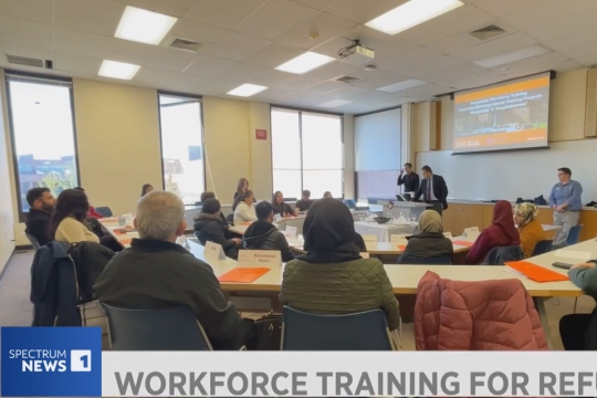 refugees sit in a classroom with professors from RIT who are shown explaining fundamentals of hospitality.