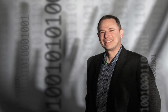 Evan Selinger appears in front of a gray backdrop wearing a black and gray suit.