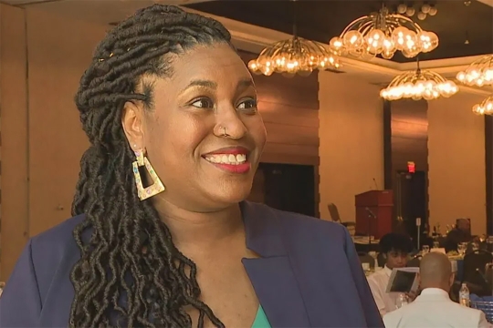 Katrina Overby is shown in a banquet hall speaking to a member of the media.