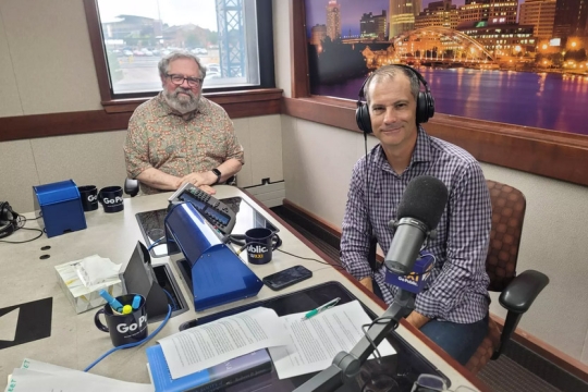 David Cay Johnston and Evan Dawson appear in a radio studio with headphones on.