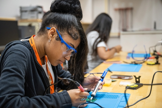 a student  uses a desoldering pump to remove excess solder while making a circuit board.