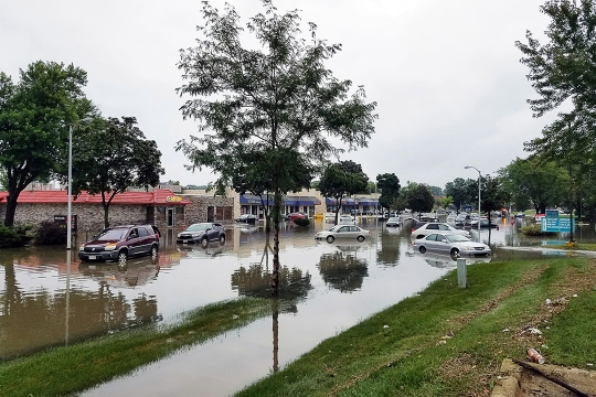 the main street of a small town appears flooded by water, with cars partially submerged.