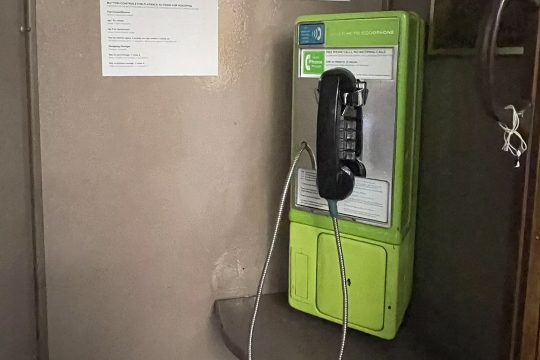 a green payphone is shown in a booth with beige walls.
