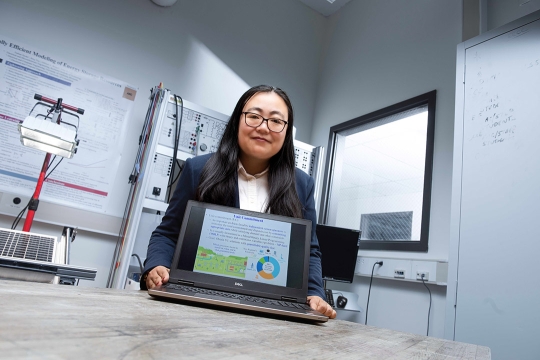 Bing Yan holds a laptop in front of themselves in a lab room.