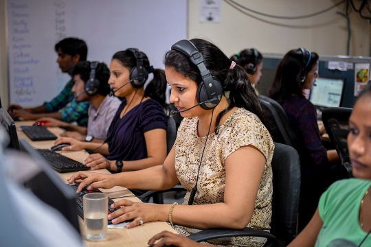 Indian females sit in an open work environment with a phone headset.