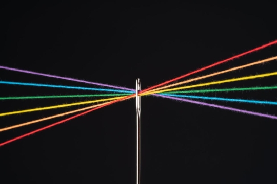 Different colors of yarn run through the eye of a needle against a black background