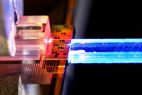 Close-up of a photonic chip emitting a bright blue laser beam.