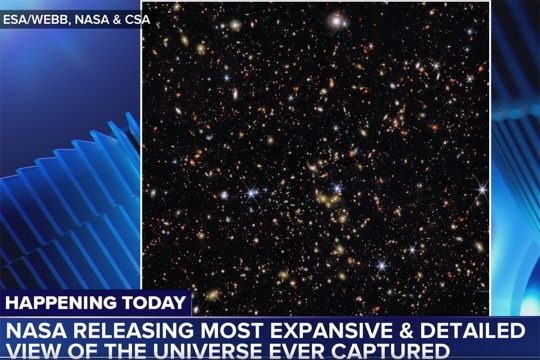 A news graphic showing a photo from the James Webb Space Telescope, which shows a smattering of brightly colored stars and galaxies against the black backdrop of the universe. The news graphic along the bottom of the screen reads, Happening today, NASA releasing most expansive and detailed view of the universe ever captured.