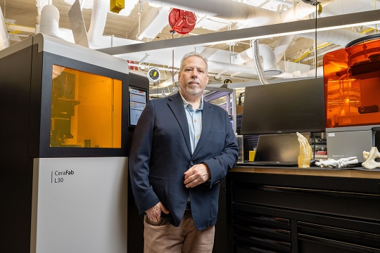 Engineer stands beside a CeraFab L30 3D printer in a lab.