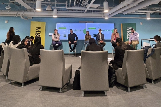 students seated in gray chairs forming a semicircle look at mentors sitting on a panel discussing their jobs.