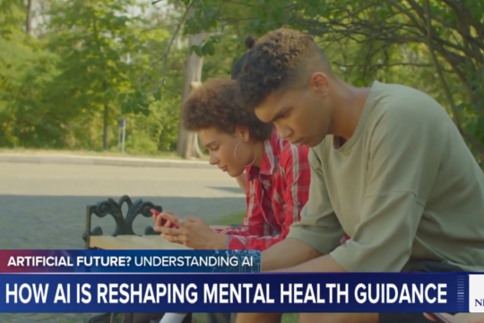 two people sit on a bench looking at their phones. Below, a chyron with the article title is displayed.